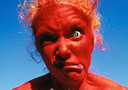 nude_woman_wearing_red_body_paint_making_face_outdoors_700-00054203