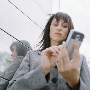 Business woman standing outside in front of office building, using mobile phone --- Image by © Royalty-Free/Corbis