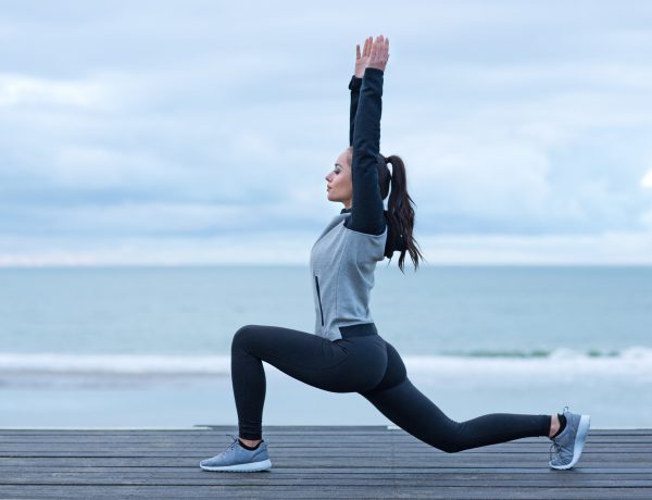 Beautiful brunette woman stretching on a seafront wearing sports clothes as a warming up exercise