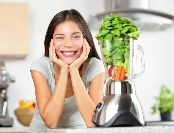 Green smoothie woman making vegetable smoothies with blender. Healthy eating lifestyle concept portrait of beautiful young woman preparing drink with spinach, carrots, celery etc at home in kitchen.
