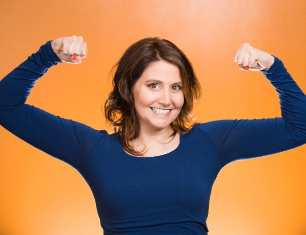 Closeup portrait beautiful, pretty model woman flexing muscles showing, displaying her strength, isolated orange background. Positive human emotions, facial expressions, feelings, attitude, perception
